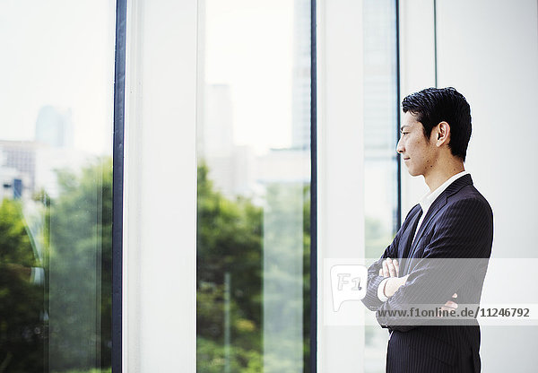 A businessman in the office  by a large window  looking out.