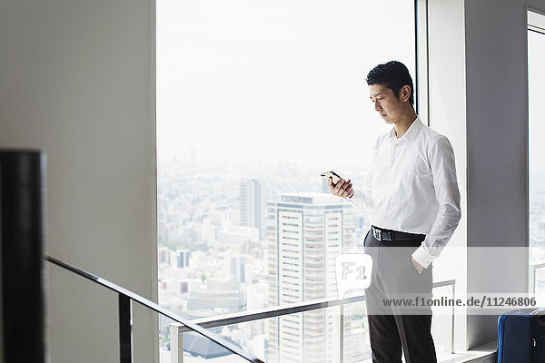 A businessman in the office  by a large window  looking at his smart phone.