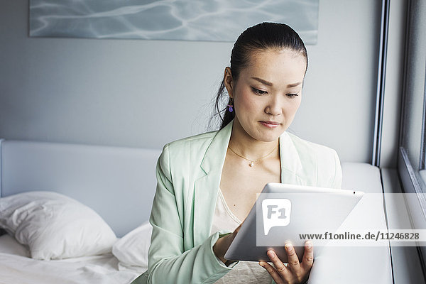 Eine Geschäftsfrau  die sich auf die Arbeit vorbereitet und mit einem digitalen Tablett auf einem Bett sitzt.