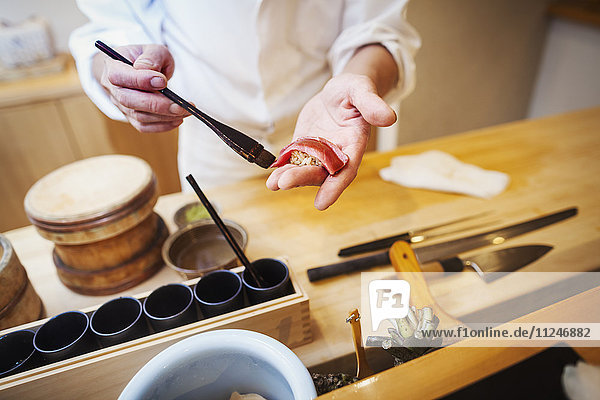 Ein Küchenchef  der in einer kleinen Großküche arbeitet  ein Itamae oder Meisterkoch  der Sushi zubereitet und Sauce auf Fisch tut.