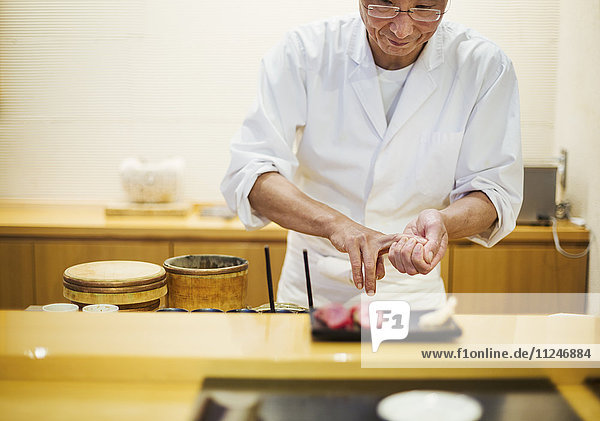 Ein Koch,  der in einer kleinen Großküche arbeitet,  ein Itamae oder ein Meisterkoch,  der einen frischen Sushi-Teller präsentiert.