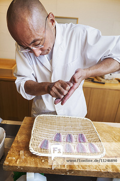 A chef working in a small commercial kitchen  an itamae or master chef making sushi  preparing fish.
