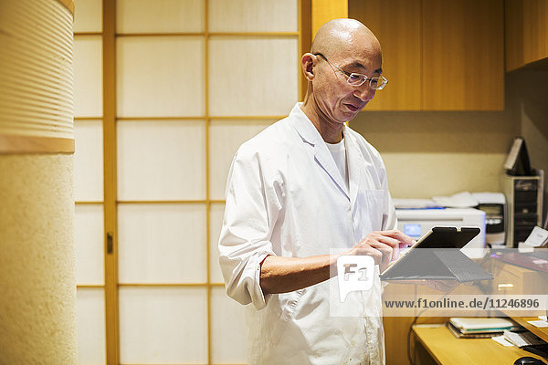 A chef in a small commercial kitchen  an itamae or master chef using a digital tablet.