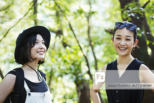 Zwei lächelnde junge Frauen stehen in einem Wald.