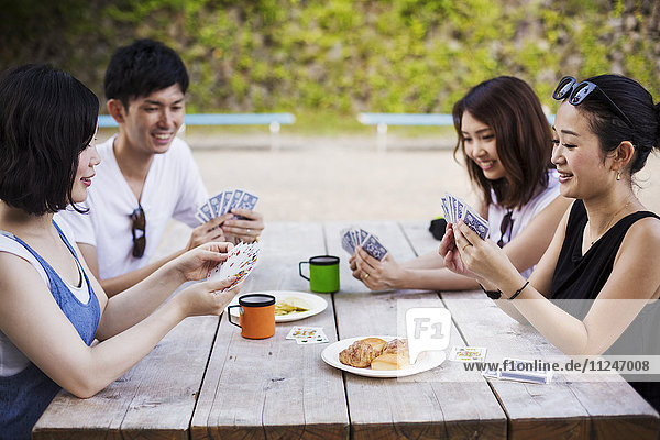Drei junge Frauen und ein Mann sitzen an einem Tisch und spielen Karten.