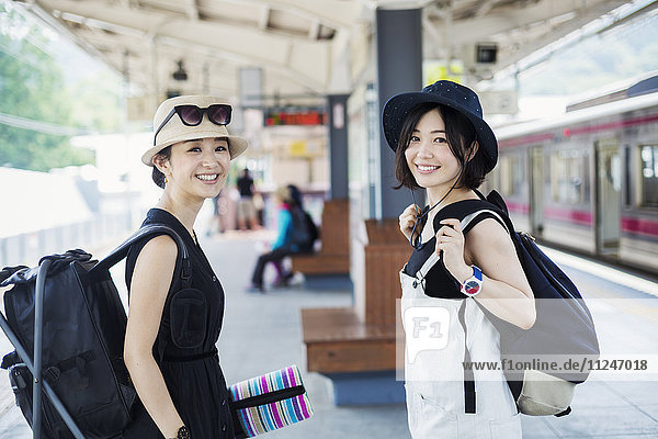 Zwei junge Frauen stehen auf einem Bahnsteig in einem Bahnhof.
