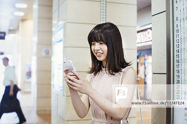 Lächelnde junge Frau mit langen braunen Haaren  die ein Mobiltelefon in der Hand hält.