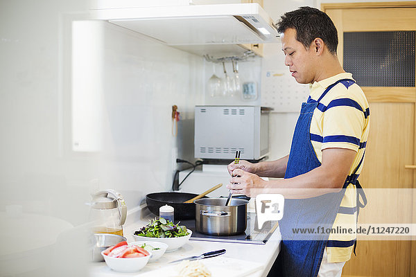 Family home. A man in a blue apron preparing a meal.