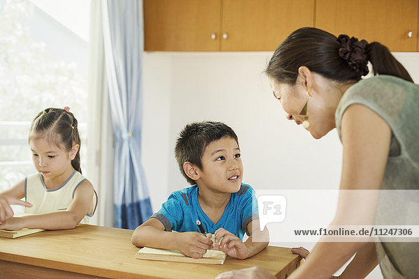 A teacher talking to two children sitting at a desk.