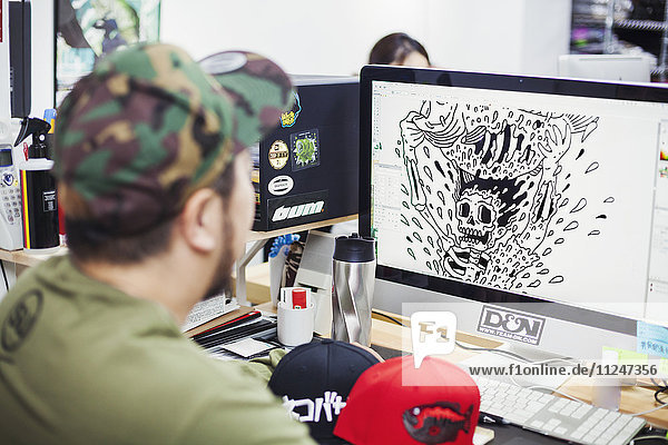 Design-Studio. Ein Mann sitzt an einem Schreibtisch und entwirft am Computer T-Shirt-Drucke.