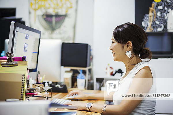 Design-Studio. Eine Frau  die an einem Schreibtisch sitzt und einen Computer benutzt.