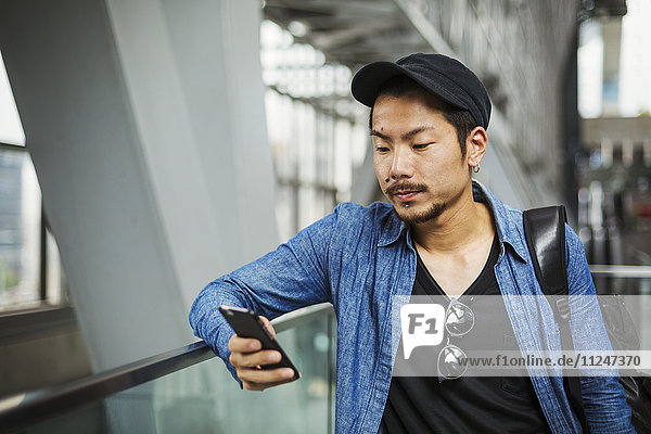 Ein Mann in einer blauen Jacke in einem modernen Gebäude mit seinem Smartphone.