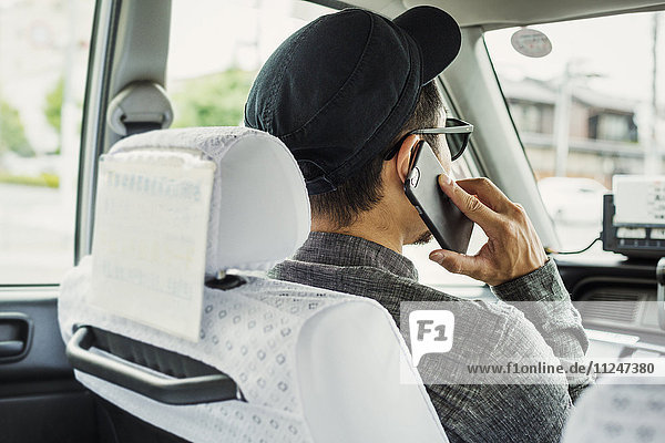 Ein Mann  der auf dem Beifahrersitz eines Autos sitzt und sein Smartphone benutzt.