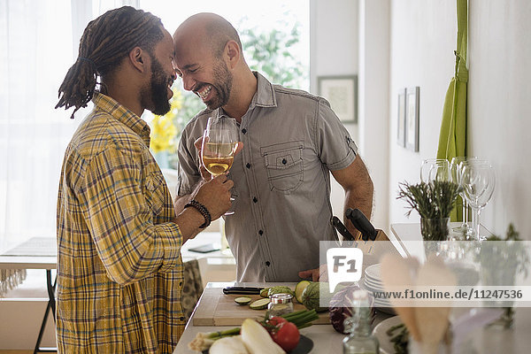 Lächelndes homosexuelles Paar trinkt Wein in der Küche