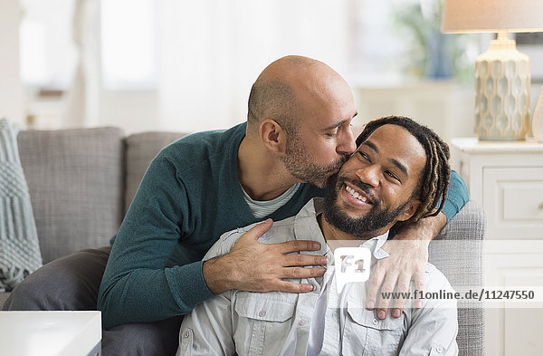 Homosexuelles Paar küsst sich auf dem Sofa im Wohnzimmer
