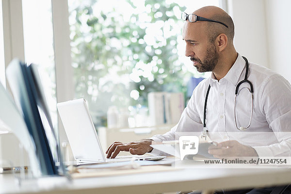 Concentrated doctor working with laptop at desk in office