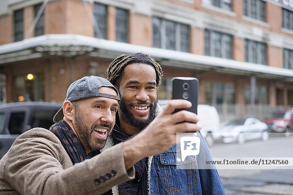 Lächelndes homosexuelles Paar  das ein Selfie mit einem Smartphone auf der Straße macht