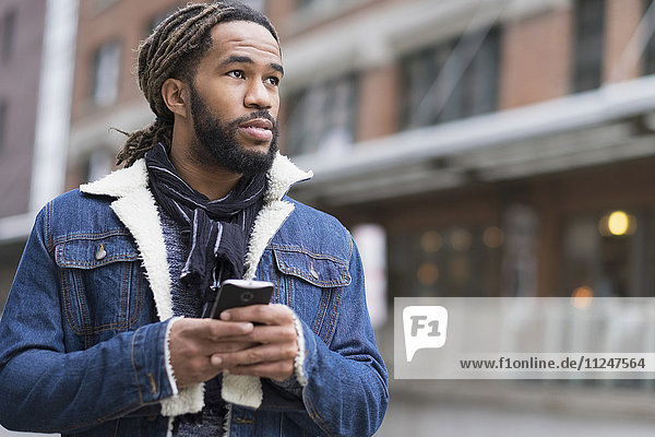 Serious man with dreadlocks holding smart phone in street