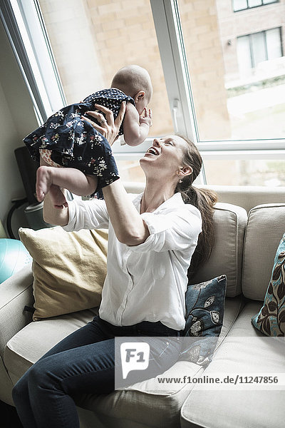 Mother playing with baby daughter (2-5 months) in living room