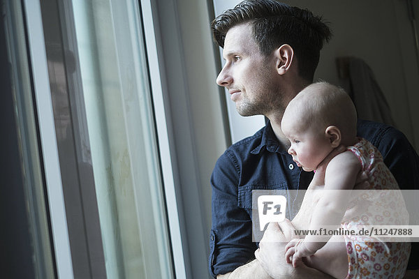Vater schaut mit Tochter durch das Fenster (2-5 Monate)
