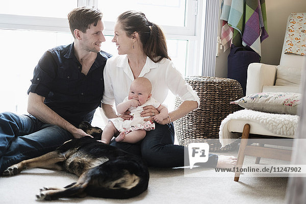 Portrait of happy family sitting on carpet with daughter (2-5 months) and dog
