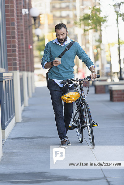 Man walking with bicycle using phone