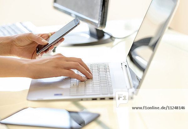 Geschäftsfrau  die eine SMS schreibt und auf einer Laptop-Tastatur tippt