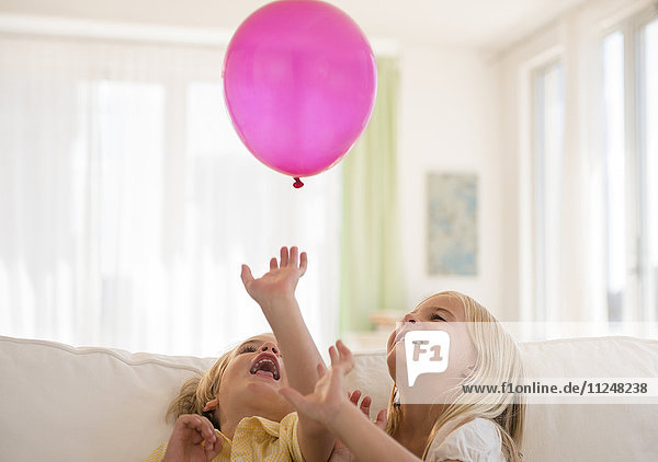 Junge (4-5) und Mädchen (6-7) spielen mit rosa Luftballon