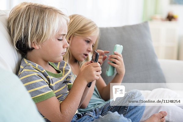 Junge (4-5) und Mädchen (6-7) spielen Spiele auf Smartphones