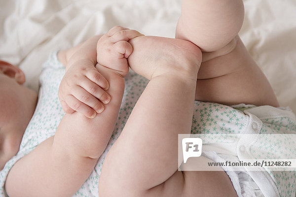 Kleines Mädchen (12-17 Monate) im Liegen mit den Händen auf den Füßen