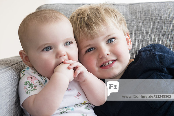 Junge (2-3) mit kleiner Schwester (12-17 Monate) auf dem Sofa sitzend