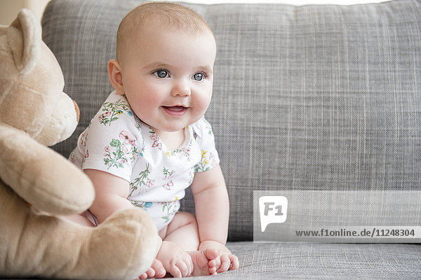 Kleines Mädchen (12-17 Monate) mit Teddybär auf dem Sofa sitzend