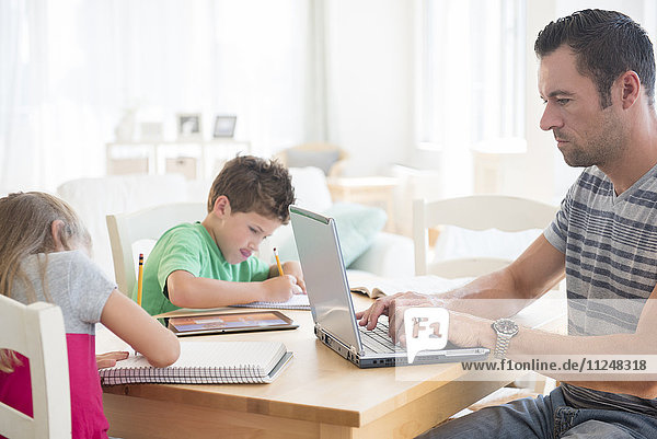Man using laptop with two children (6-7  8-9) writing in notepads