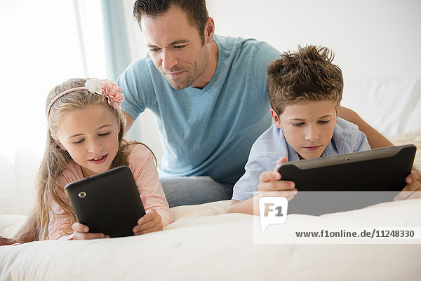 Father with son (8-9) and daughter (6-7) using tablets