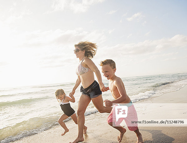 Mother running with boy (6-7) and girl (4-5) on beach by water