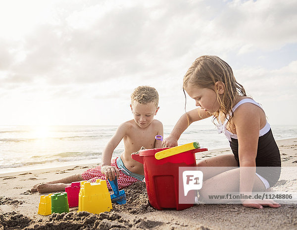Junge (6-7) und Mädchen (4-5) spielen mit Sand am Strand