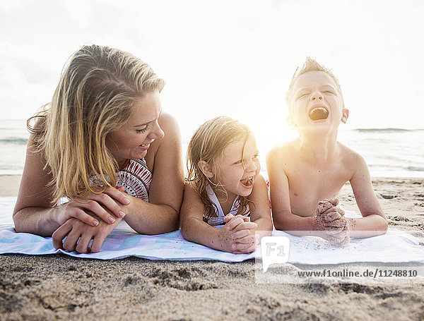 Mother lying down with son (6-7) and daughter (4-5) on beach