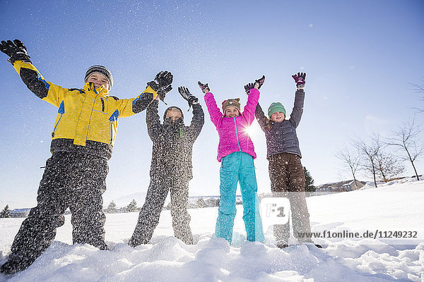 Children (8-9 10-11) standing in snow with arms raised