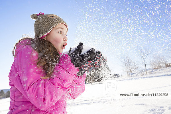 Girl (10-11) in pink jacket blowing snow