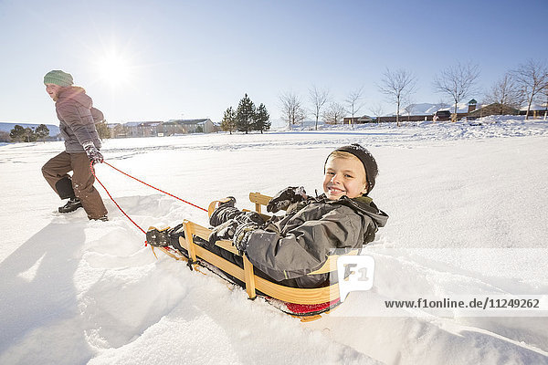 Children (8-9) playing with sled in snow