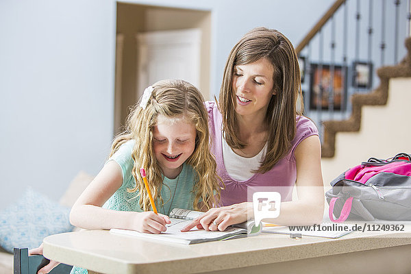 Mutter und Tochter (8-9) sitzen am Tisch und machen Hausaufgaben