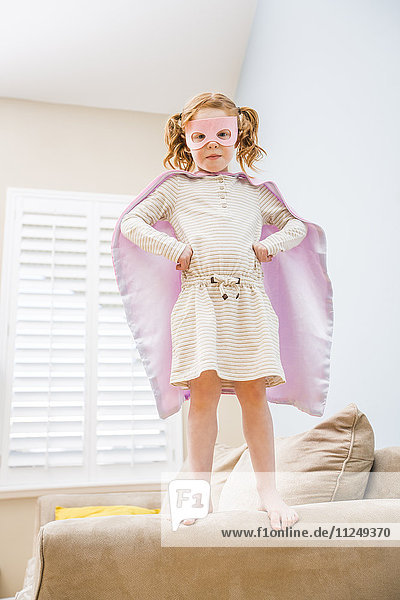 Little girl (4-5) playing superman on sofa