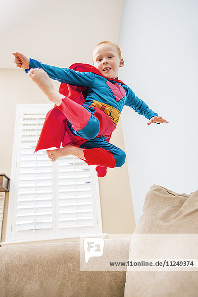 Little boy (2-3) in superman costume jumping on sofa