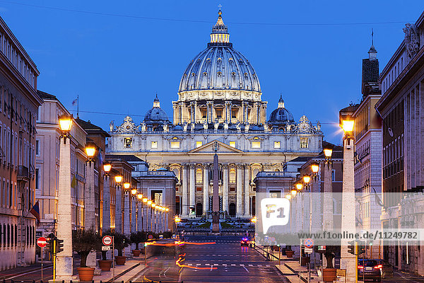 Beleuchteter Petersdom mit asphaltierter Straße im Vordergrund in der Abenddämmerung
