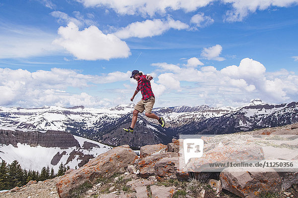 Mid adult man jumping over rocks in mountains