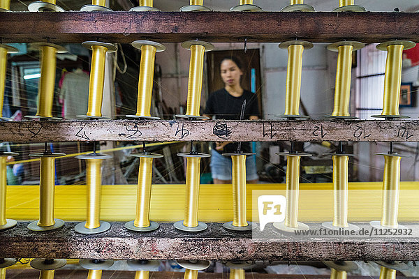 A silk weaver creates a bolt of gold thread at a traditional workshop in Bangkok  Thailand  Southeast Asia  Asia