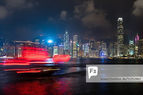 A red junk sailboat glides in front of the Hong Kong skyline at night  Hong Kong  China  Asia