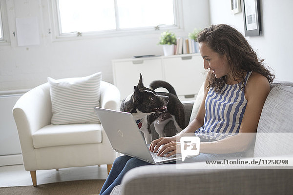 Junge Frau sitzt mit Laptop und Hund auf dem Sofa