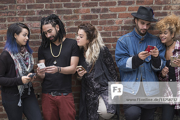 Portrait of friends using smartphones against brick wall