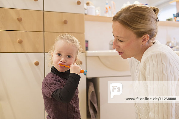 Mother looking at daughter (4-5) brushing teeth in bathroom